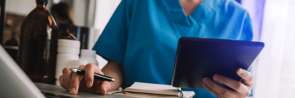 Eine Ärztin sitzt an einem Tisch und arbeitet mit Laptop und Tablet.